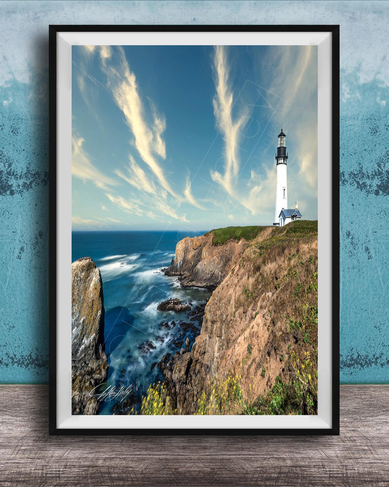 A framed photograph of a lighthouse on a cliff overlooking the ocean, with a blue sky and wispy clouds in the background.
