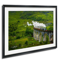 A steam train travels along a curved stone bridge in a lush, green landscape.