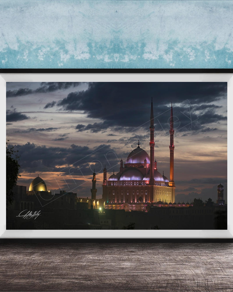 A framed photograph of a mosque at night, with its illuminated domes and minarets standing against a dark sky with clouds.
