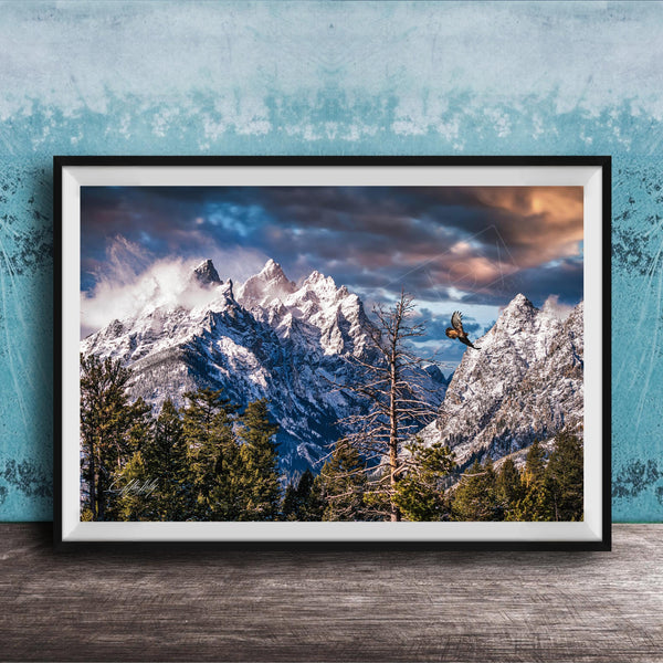 A framed photograph of a snow-capped mountain range with a cloudy sky, surrounded by pine trees and a lone bird in flight.