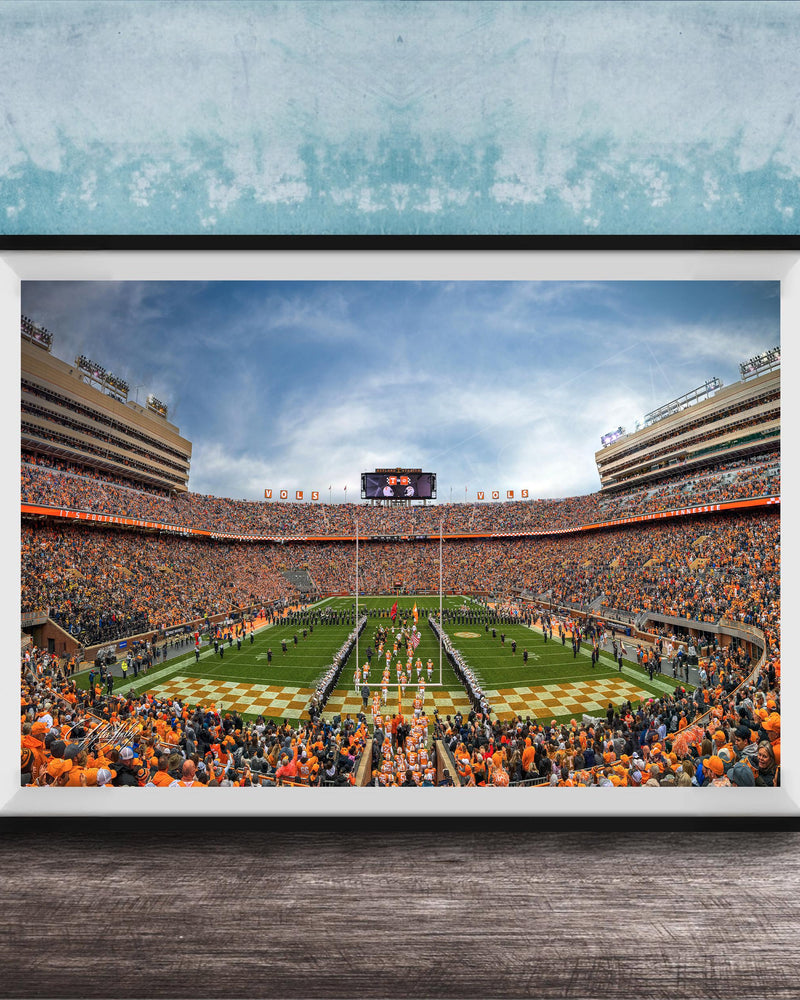 A framed photograph of a crowded football stadium during a game, with the field and stands filled with spectators.