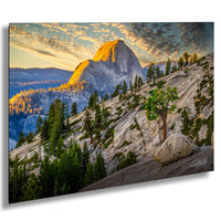 a breathtaking mountain landscape with a large, snow-capped peak in the background, surrounded by a lush forest of evergreen trees. The sun is setting, casting a warm, golden glow over the scene and illuminating the rocky terrain.