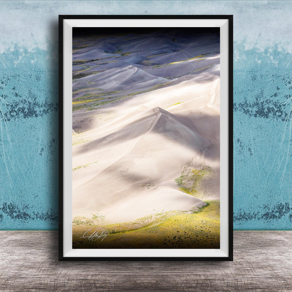 The image is a framed photograph of a mountainous landscape with white sand dunes and patches of green vegetation.