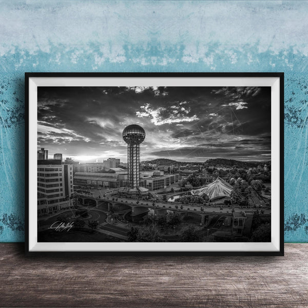 A black and white photograph of a cityscape, featuring a tall tower, a bridge, and other buildings, set against a cloudy sky.