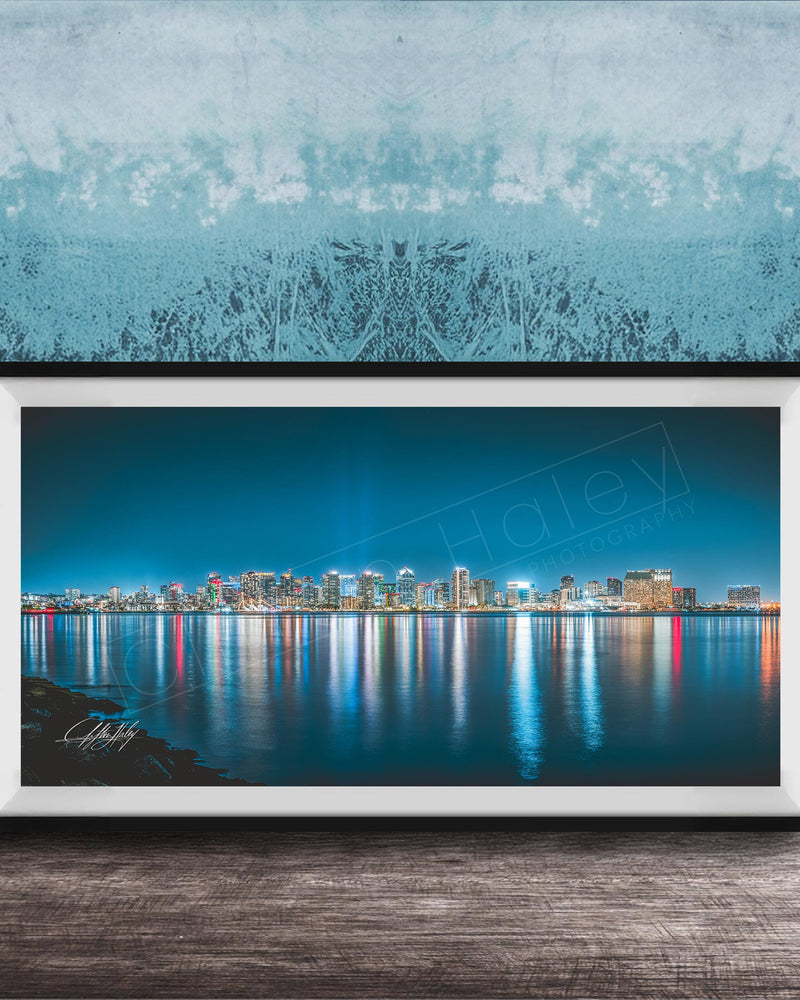 A framed photograph of a city skyline at night, with the buildings' lights reflected in the water below.