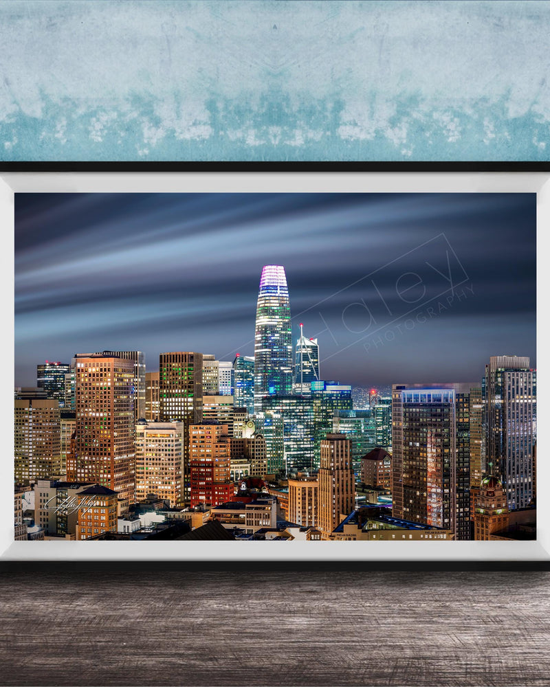 A framed photograph of a city skyline at night, with numerous illuminated skyscrapers and buildings against a dark sky.