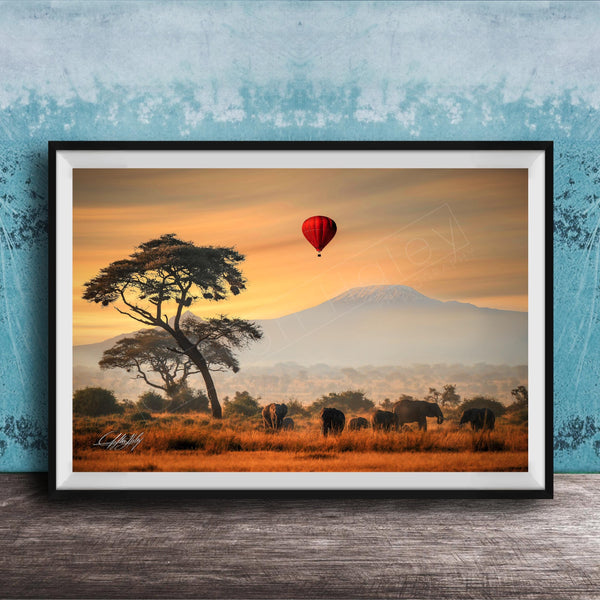 A framed photograph depicting a serene landscape with a lone tree, a herd of elephants, and a red hot air balloon floating in the sky, all set against a backdrop of a majestic mountain range.