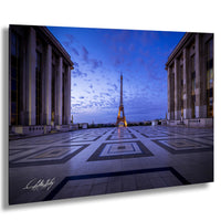 the Eiffel Tower in Paris, France, with its iconic structure illuminated against a dark blue sky. The photograph is taken from a low angle, emphasizing the tower's height and grandeur. The square-shaped plaza in the foreground adds to the overall composition of the image.