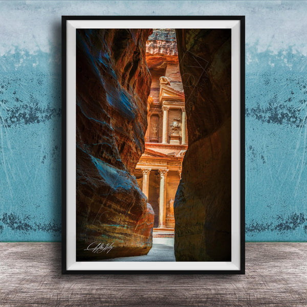 A framed photograph of a narrow passage between two large rock formations, with a building visible through the opening.