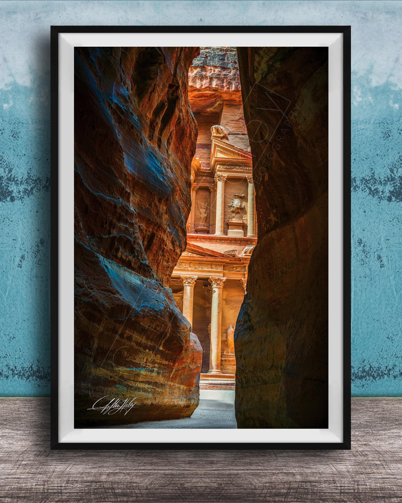 A framed photograph of a narrow passage between two large rock formations, with a building visible through the opening.