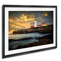 A framed photograph depicting a lighthouse on a rocky coastline at sunset, with the sky filled with clouds and the ocean in the background.