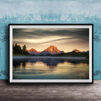 A framed photograph depicting a serene mountain landscape at sunset, with a calm lake reflecting the warm colors of the sky.