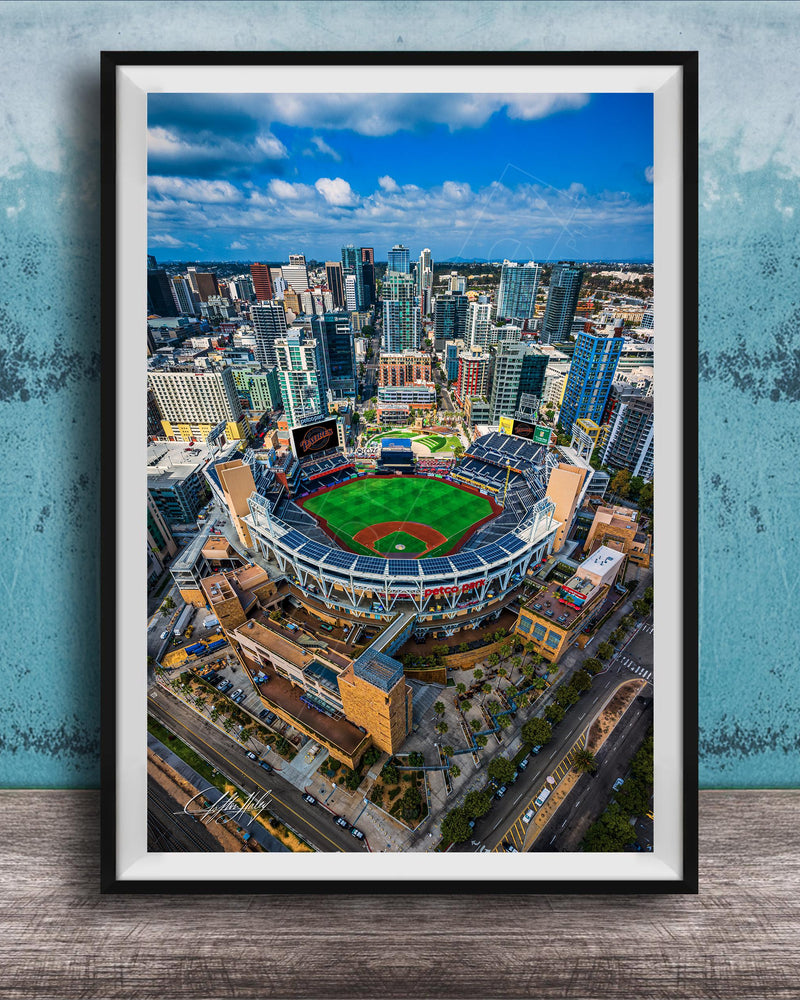 An aerial view of a baseball stadium surrounded by a city skyline, with tall buildings and a clear blue sky in the background.