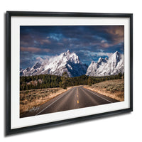 A framed photograph depicting a scenic mountain landscape with a winding road leading towards the majestic peaks.
