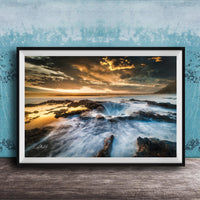 The image is a framed photograph of a rocky coastline with crashing waves, set against a dramatic sky with clouds and a sunset.