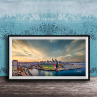 The image is a framed photograph of a cityscape at sunset, featuring a skyline with tall buildings and a body of water in the foreground.