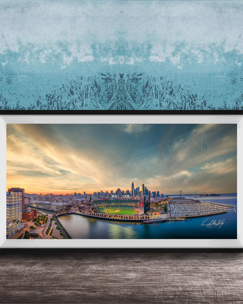 The image is a framed photograph of a cityscape at sunset, featuring a skyline with tall buildings and a body of water in the foreground.