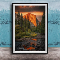 a breathtaking view of a mountain range at sunset, with the sun's warm glow illuminating the peaks and casting a vibrant orange and red hue across the sky. The foreground features a river flowing through the landscape, with rocks and trees lining its banks. The overall composition is visually striking and evokes a sense of tranquility and natural beauty.