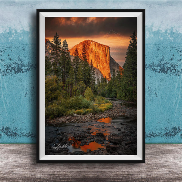 a breathtaking view of a mountain range at sunset, with the sun's warm glow illuminating the peaks and casting a vibrant orange and red hue across the sky. The foreground features a river flowing through the landscape, with rocks and trees lining its banks. The overall composition is visually striking and evokes a sense of tranquility and natural beauty.