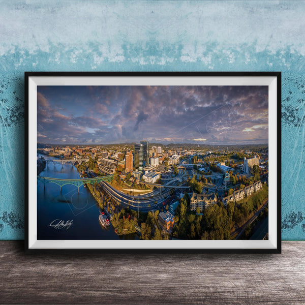 The image is a framed aerial view of a cityscape, showcasing a mix of buildings, roads, and a river.
