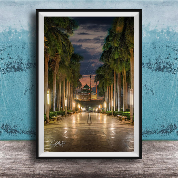 A framed photograph depicting a serene nighttime scene of a palm-lined walkway leading towards a building with a dome, illuminated by warm lighting.