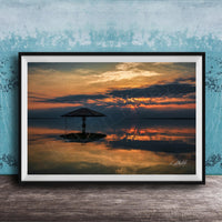 A framed photograph depicting a serene sunset over a calm body of water, with a lone umbrella standing in the foreground.