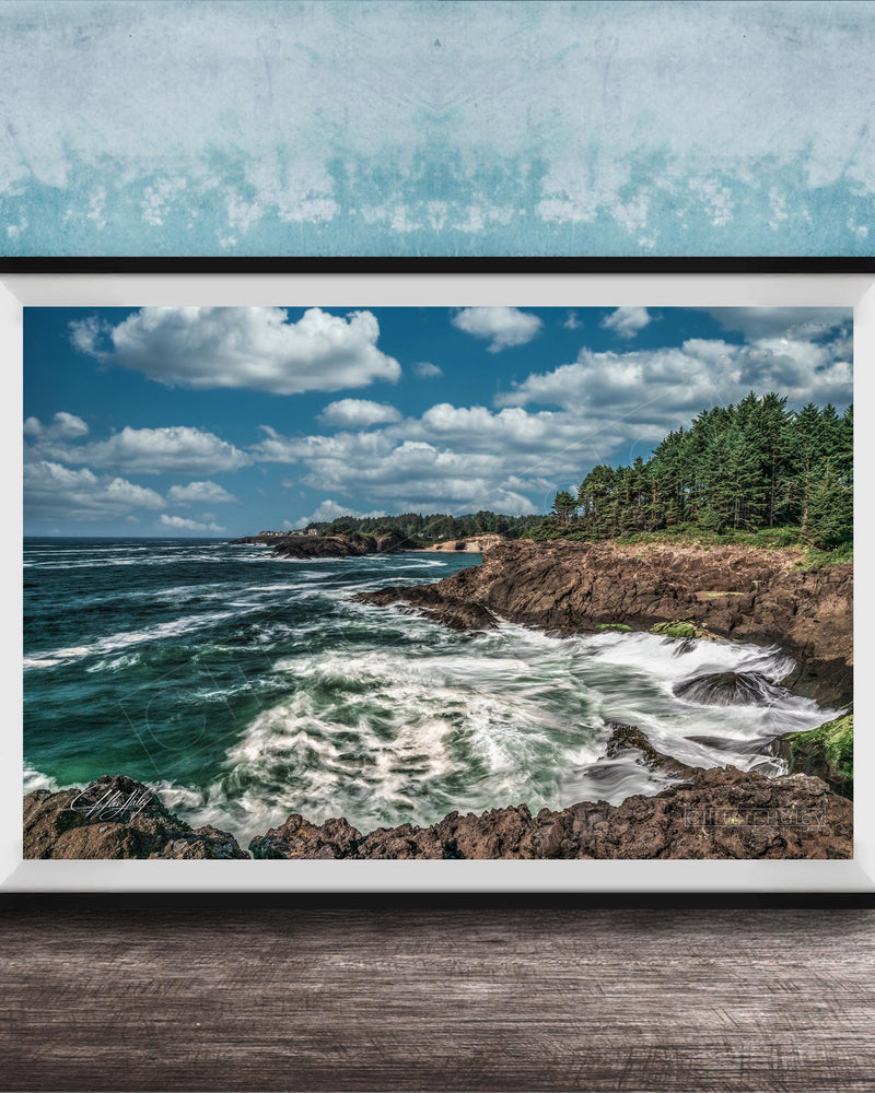 A framed photograph of a rocky coastline with crashing waves, set against a backdrop of a blue sky with fluffy white clouds.