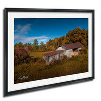 a rustic wooden barn nestled in a lush, green field, surrounded by trees with vibrant autumn foliage.