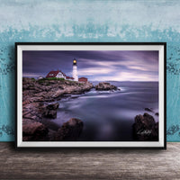 A framed photograph of a lighthouse on a rocky shore, with the ocean and a cloudy sky in the background.
