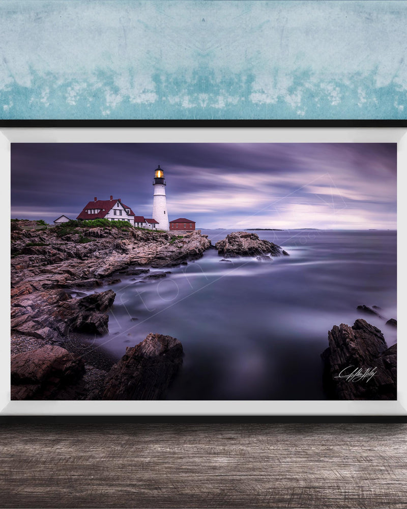 A framed photograph of a lighthouse on a rocky shore, with the ocean and a cloudy sky in the background.