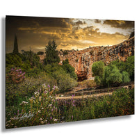 a scenic landscape with a rocky cliff face, lush vegetation, and a winding path leading through the area. The sky is filled with clouds, creating a dramatic backdrop for the natural setting.