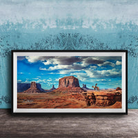 A framed painting depicting a scenic desert landscape with a person riding a horse in the foreground, set against a backdrop of mountains and a blue sky with clouds.