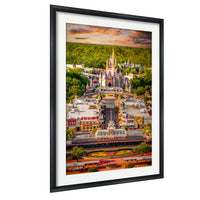 A framed aerial view of a colorful and ornate castle-like structure surrounded by lush greenery and a vibrant sky.
