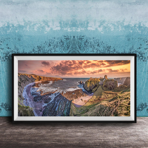 The image is a framed photograph of a scenic coastal landscape with rugged cliffs, a rocky shoreline, and a dramatic sunset over the ocean.