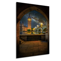 a night scene of the Palace of Westminster and the Elizabeth Tower, also known as Big Ben, in London, England. The clock tower is illuminated against a starry sky, with the River Thames visible in the foreground. The scene is captured through an archway, creating a sense of depth and perspective.