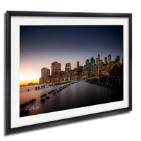 A framed photograph of the New York City skyline at dusk, with the city's iconic skyscrapers illuminated against the darkening sky.