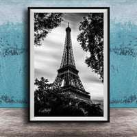A black and white photograph of the Eiffel Tower, a famous landmark in Paris, France, framed and displayed on a wooden surface against a blue textured background.