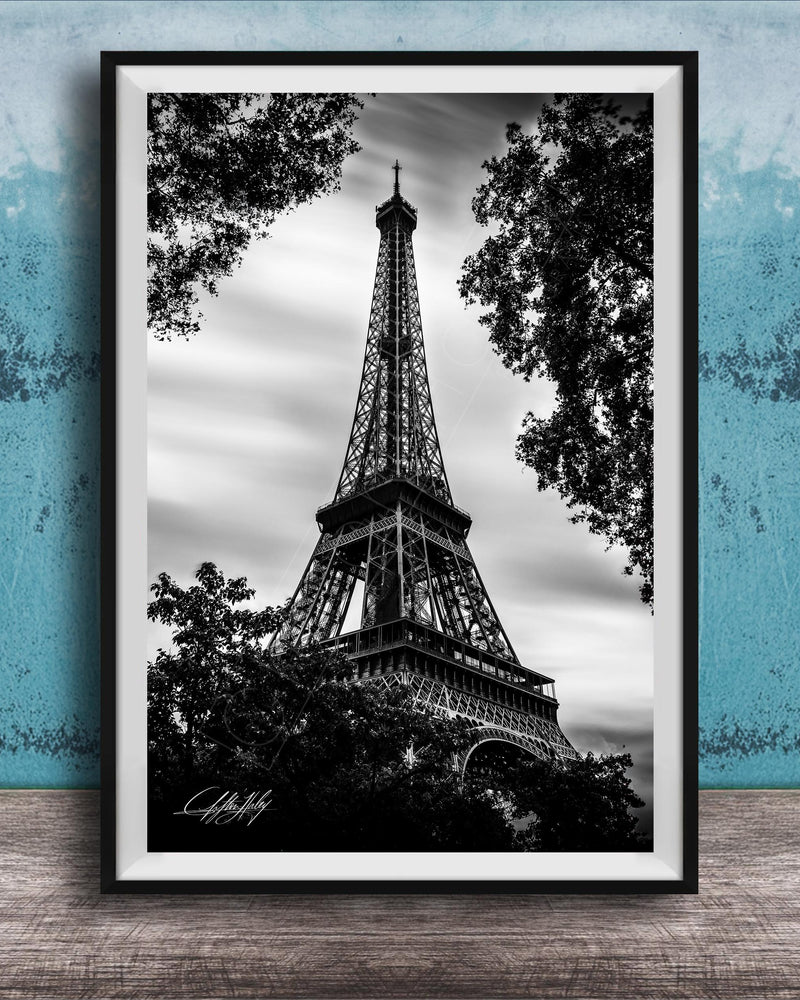 A black and white photograph of the Eiffel Tower, a famous landmark in Paris, France, framed and displayed on a wooden surface against a blue textured background.