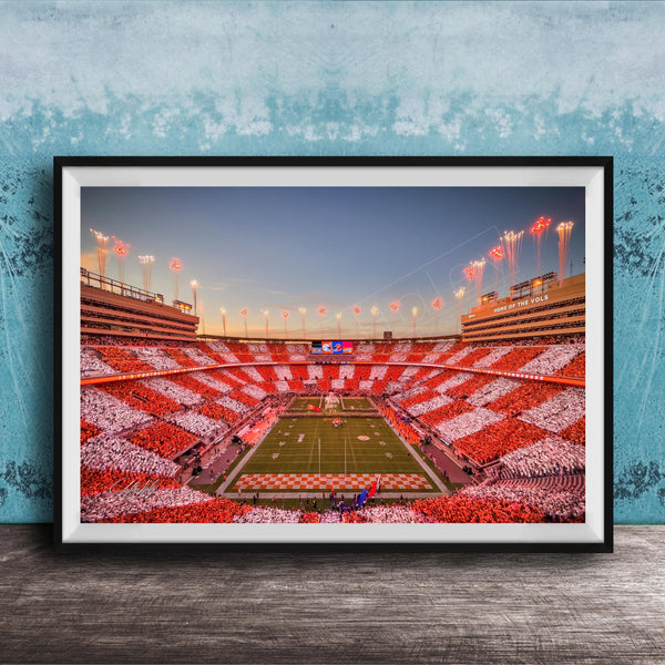A framed photograph of a football stadium at night, with the field illuminated by red and white lights and the stands filled with spectators.