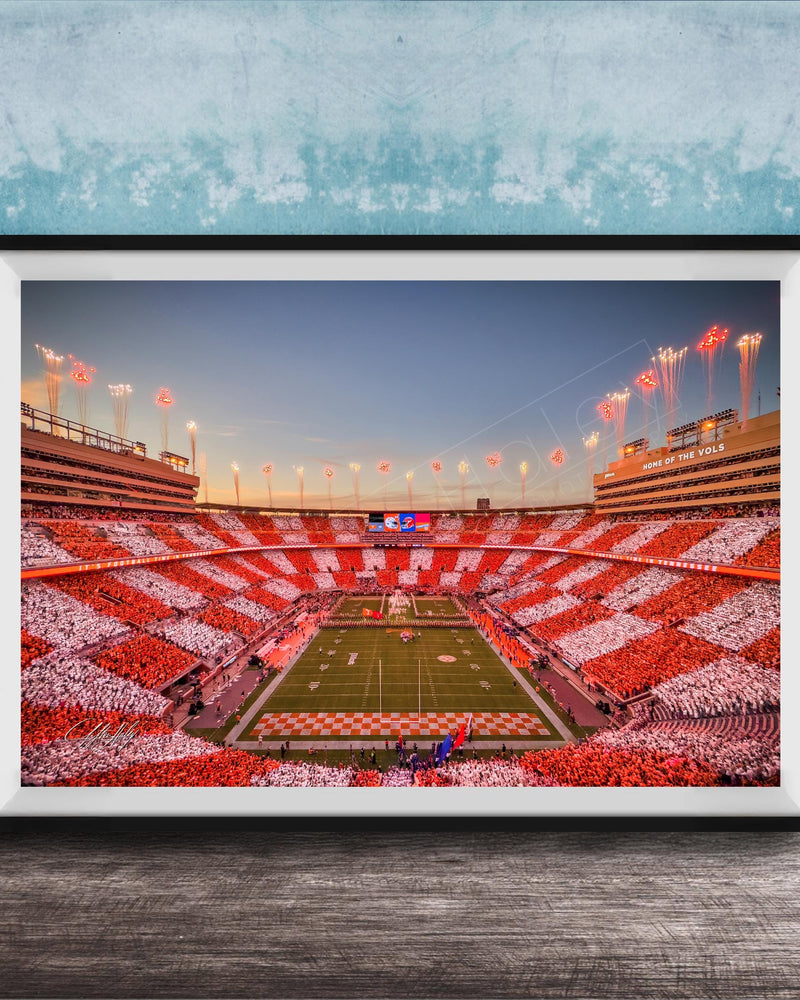 A framed photograph of a football stadium at night, with the field illuminated by red and white lights and the stands filled with spectators.