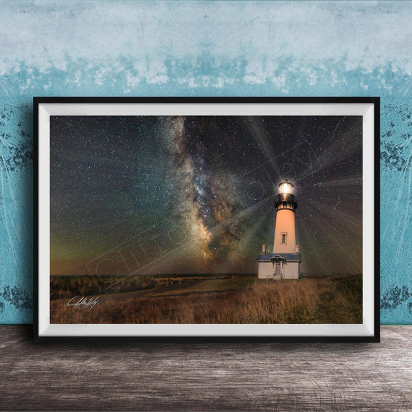 A framed photograph depicting a lighthouse standing in a field at night, with a starry sky and a galaxy in the background.