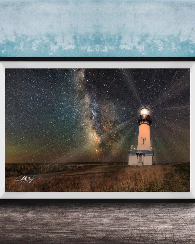 A framed photograph depicting a lighthouse standing in a field at night, with a starry sky and a galaxy in the background.