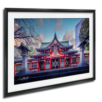 A framed photograph of a traditional Japanese temple with a red roof and white walls, surrounded by trees and a building in the background.