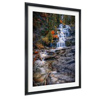 A framed photograph depicting a waterfall cascading down a rocky cliff surrounded by trees with autumn foliage.