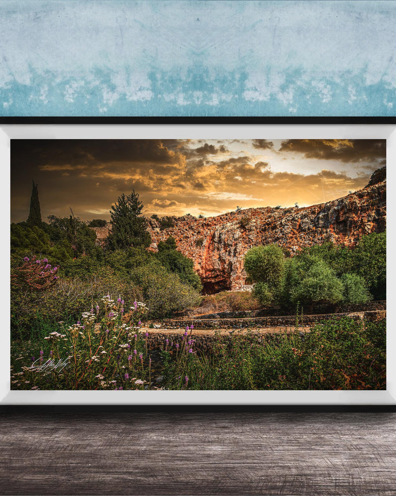 The image is a framed photograph depicting a scenic landscape with a rocky cliff, lush vegetation, and a dramatic sky with clouds.