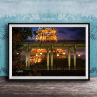 A framed photograph of the Eiffel Tower at night, with the tower illuminated and surrounded by trees and a bridge.