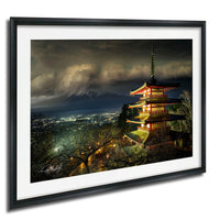 A framed photograph depicting a traditional Japanese pagoda illuminated at night, with a mountainous landscape in the background.