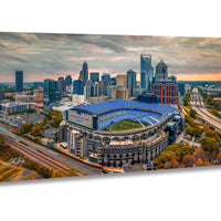 An aerial view of a large stadium with a blue roof, surrounded by a city skyline with tall buildings and skyscrapers.