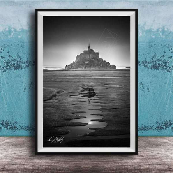 A black and white photograph of a castle or palace situated on a beach, with a body of water in the foreground and a sky above.