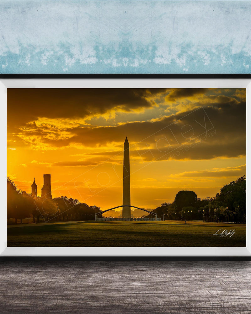 the Washington Monument at sunset, with the tall obelisk silhouetted against a vibrant orange and yellow sky.